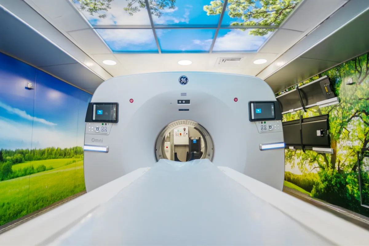 PET/CT scanner inside an SMS mobile unit with nature-themed walls and ceiling.