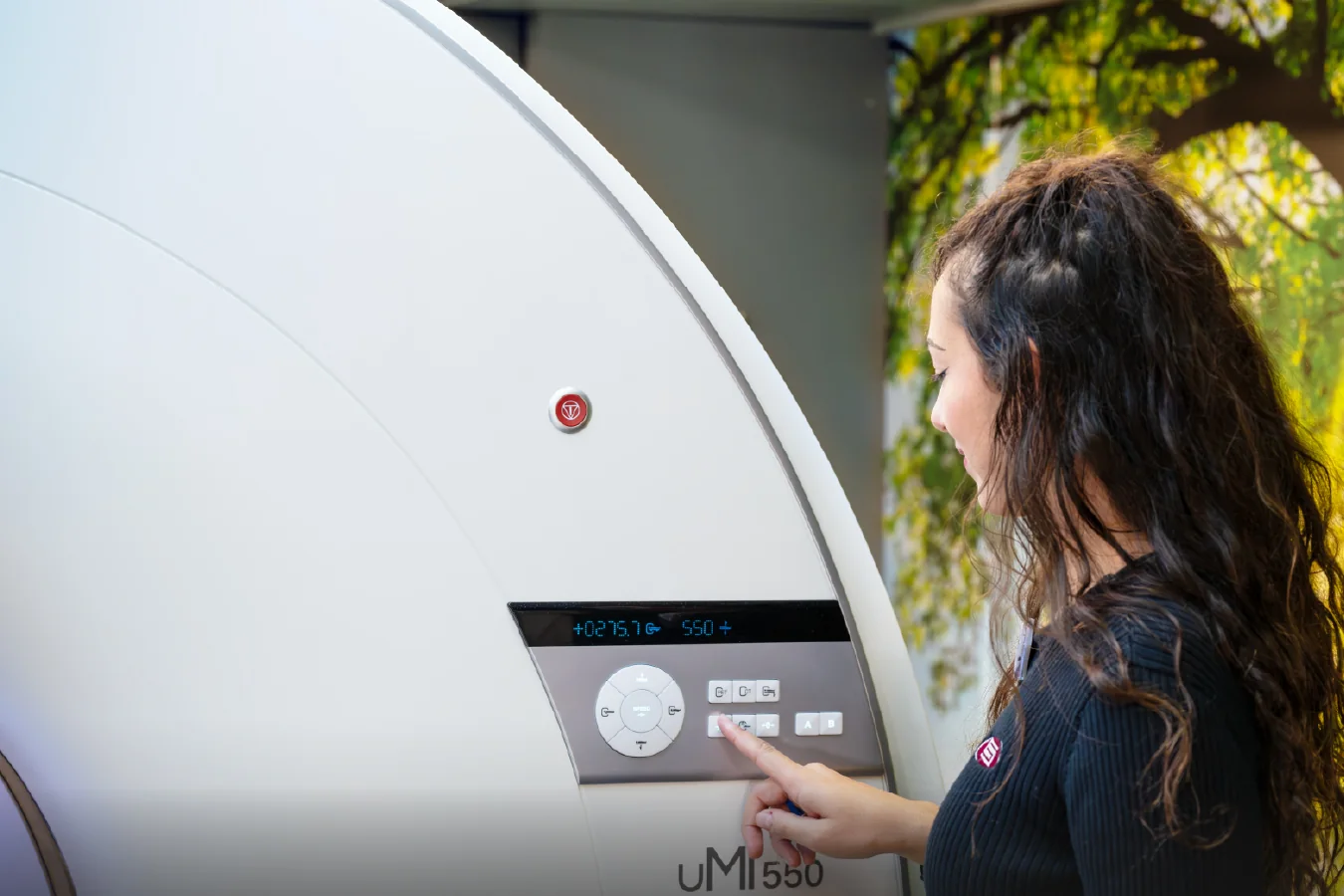 An SMS technologist operating the controls beside a United Imaging uMI 550 PET/CT scanner.